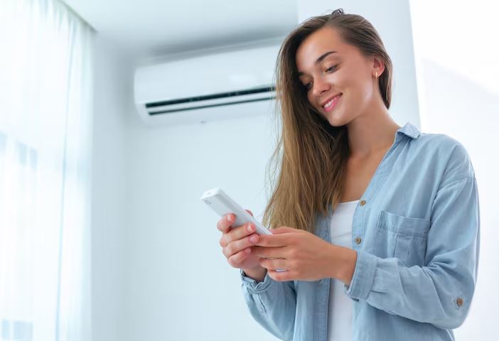 pessoa ajustando ar-condicionado em quarto à noite com controle remoto, buscando conforto térmico sem ruído excessivo