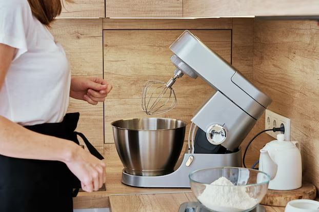 Melhor Batedeira planetária inox sobre bancada de cozinha com ingredientes para bolo ao redor, pronta para uso.