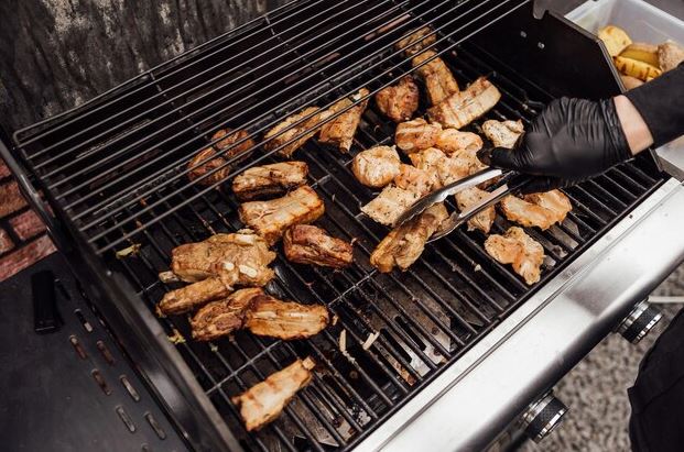 Churrasqueira elétrica sobre bancada em varanda de apartamento, grelha com carnes e legumes sendo preparados