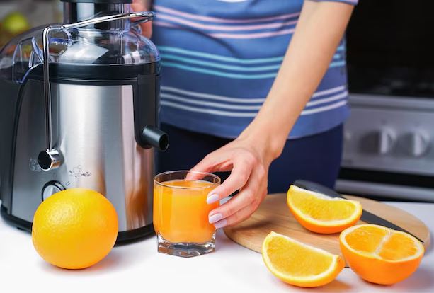 Espremedor de frutas moderno sobre a bancada de cozinha ao lado de copos com suco fresco.