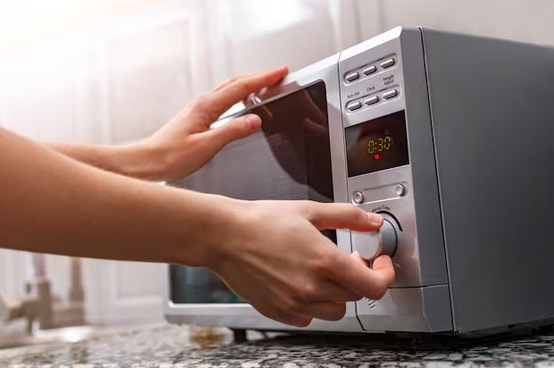 Melhor Micro-ondas moderno em bancada de cozinha planejada, com painel aceso e travessa de vidro sendo inserida