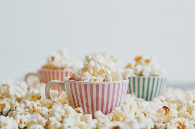 Pipoqueira elétrica ligada sobre a bancada de cozinha, com pipoca pronta transbordando para uma tigela ao lado.