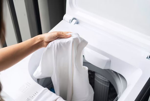 Tanquinho em uso na área de serviço residencial, com roupas sendo lavadas e balde ao lado para enxágue e drenagem.